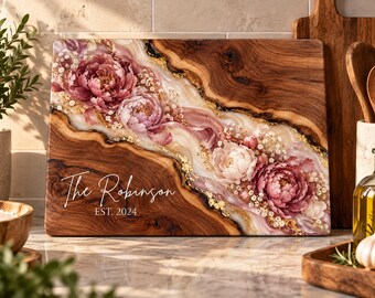 Peut inclure: Une planche à découper rectangulaire en bois avec une incrustation en résine diagonale ornée de motifs de pivoines roses et blanches, de feuilles d'or et du texte blanc "The Robinson EST. 2024" imprimé sur le côté inférieur gauche.