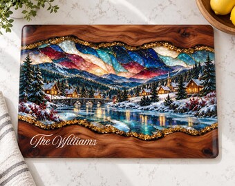 Peut inclure: Une planche à découper rectangulaire en bois présentant une scène hivernale centrale avec des maisons enneigées, des sapins et une rivière, encadrée par de la résine à paillettes dorées. Le texte The Williams est écrit en blanc.