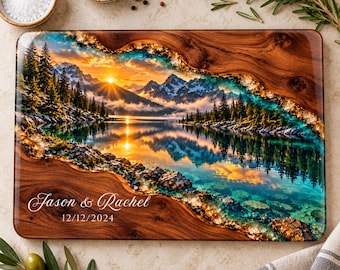 Peut inclure: Une planche à découper rectangulaire en bois avec une incrustation en résine brillante représentant un paysage de lac de montagne au coucher du soleil. Le texte Jason & Rachel et la date 12/12/2024 sont gravés en blanc.