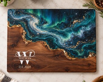 Peut inclure: Une planche à découper rectangulaire en bois avec un grain brun foncé d'un côté et un motif en résine tourbillonnant bleu sarcelle, bleu et vert avec des accents de feuilles d'or. Le texte WATSON et EST. 2024 est gravé en blanc.