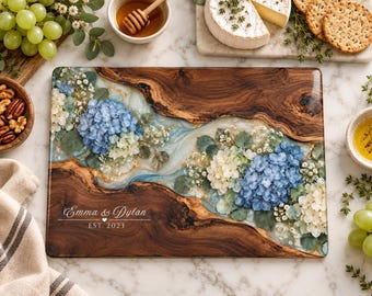Peut inclure: Une planche de service rectangulaire en bois avec une rivière centrale en résine transparente incrustée de fleurs d'hortensia bleues et blanches et de feuilles d'or. La planche porte l'inscription Emma & Dylan EST. 2023 et un grain de bois naturel.