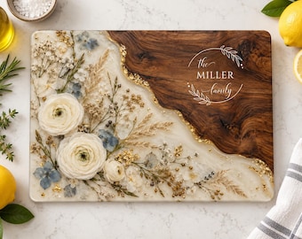 Peut inclure: Une planche de service rectangulaire composée d'une section en bois foncé et d'une section en résine crème incrustée de fleurs blanches séchées, de pétales bleus et de flocons dorés. Le bois porte le texte blanc "the MILLER family".