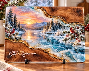 Peut inclure: Une planche à découper rectangulaire en verre illustrant un paysage hivernal avec des sapins enneigés, une rivière gelée et des montagnes au coucher du soleil. Deux cardinaux rouges sont posés sur des branches. Le texte The Robinson est inscrit.