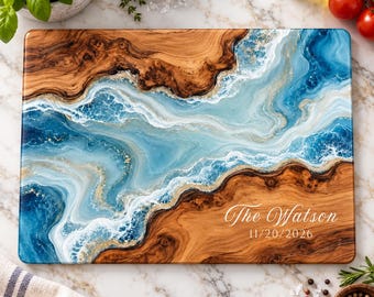 Peut inclure: Une planche de service rectangulaire en bois avec un grain naturel sur les côtés et une incrustation centrale en résine aux nuances tourbillonnantes de bleu, blanc et or. La planche porte l'inscription The Watson et la date 20/11/2026.