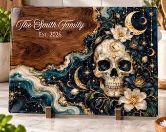 Peut inclure: Une planche à découper rectangulaire en verre avec un motif de grain de bois à gauche et un design céleste bleu foncé, doré et blanc à droite. Elle présente un crâne, des fleurs et des lunes avec le texte The Smith Family EST. 2026.