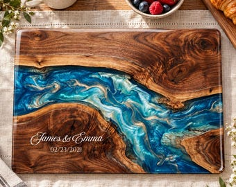 Peut inclure: Une planche de service rectangulaire en bois avec une incrustation centrale en résine bleue et blanche tourbillonnante. Le bois présente un grain naturel et la surface est gravée du texte blanc James & Emma et de la date 23/02/2021.