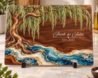 Peut inclure: Une planche à découper rectangulaire avec un motif imprimé de saule sur un fond en grain de bois foncé, agrémenté d'un effet de rivière en résine bleue et dorée. Le texte indique Jacob & Julia et EST. 2023.