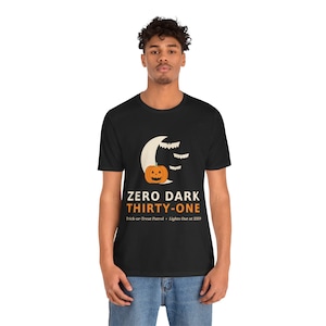 May include: A black short-sleeve t-shirt featuring a graphic of a crescent moon, three bats, and an orange jack-o'-lantern. Below the graphic, the text reads: ZERO DARK THIRTY-ONE, Trick-or-Treat Patrol, and Lights Out at 2359 in white and orange.