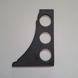 May include: A black, textured, L-shaped bracket featuring a curved outer edge and three circular cutouts arranged vertically. The object has a flat base and a straight vertical side, constructed from a rigid material with a matte finish.