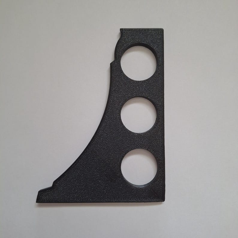 Op de afbeelding: Een zwarte, getextureerde L-vormige beugel met een gebogen buitenrand en drie verticaal geplaatste ronde uitsparingen. Het object heeft een platte basis en een rechte verticale zijde, vervaardigd uit een stijf materiaal met een matte afwerking.