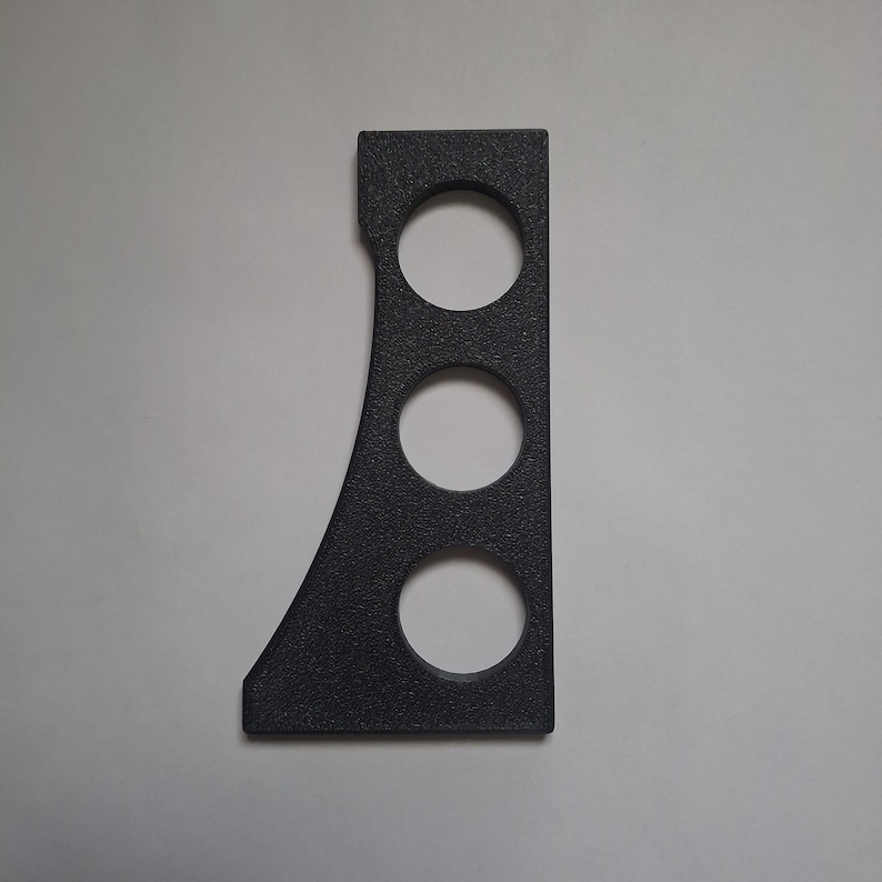 May include: A black, textured, flat, rigid component featuring a straight vertical edge on the right side and a curved edge on the left side. The object contains three circular cutouts arranged in a vertical line along its central axis.
