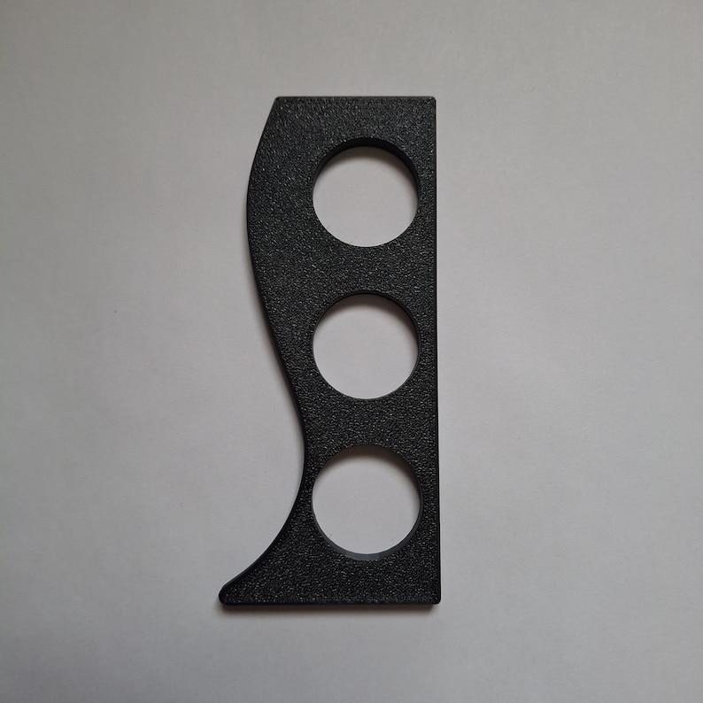 May include: A black, textured, flat object with a straight vertical edge on one side and a curved, wave-like edge on the other. The object features three circular cutouts arranged in a vertical line, creating a distinct, functional, and geometric shape.