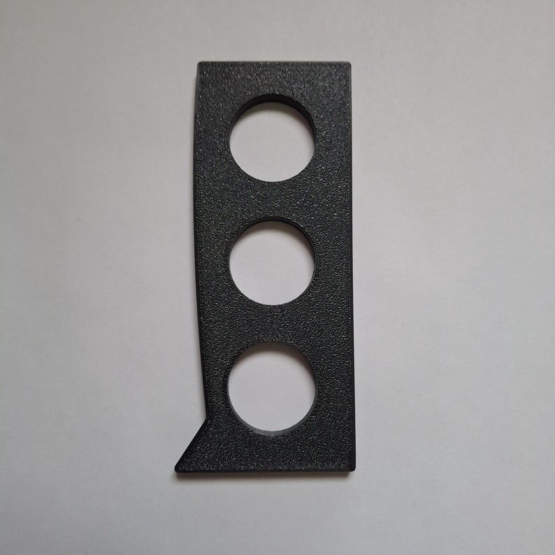 May include: A rectangular black object with a textured surface featuring three circular cutouts arranged vertically. The left side of the object has a straight edge that angles outwards at the bottom, creating a distinct corner shape.