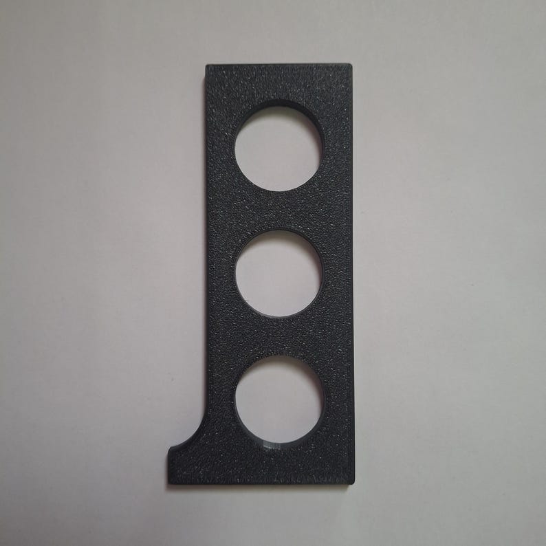 May include: A rectangular black object with a textured surface featuring three circular cutouts arranged vertically in a line. The bottom left corner of the object has a small curved indentation, creating a distinct geometric shape.