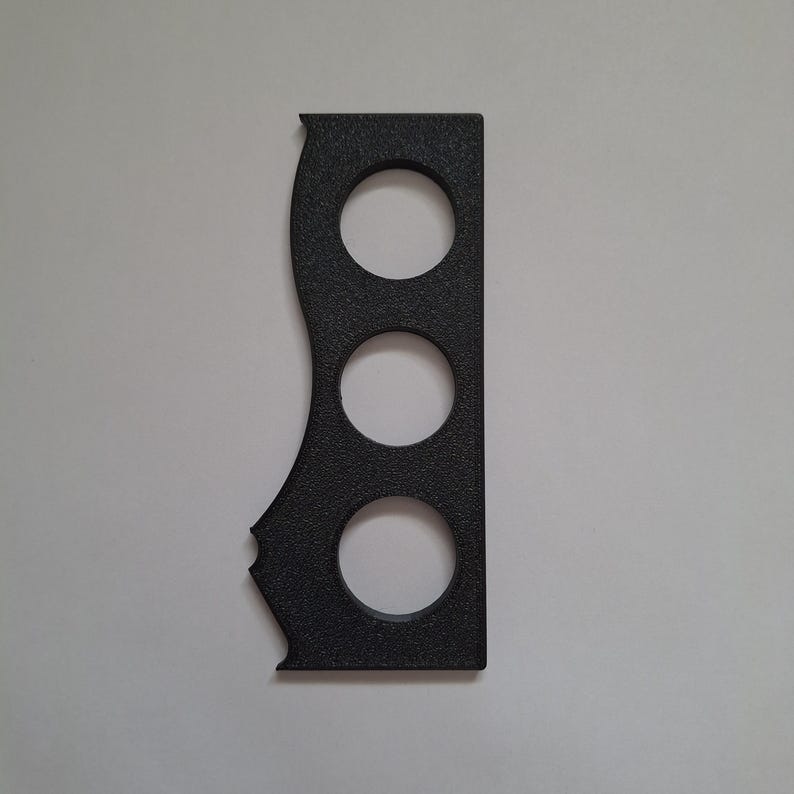 May include: A black, textured, rectangular object featuring three circular cutouts arranged vertically in the center. The left side of the object has a distinct wavy, contoured edge, while the right side remains straight and flat.