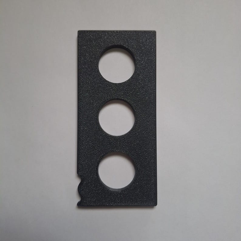 May include: A rectangular dark grey object with a textured surface featuring three evenly spaced circular cutouts arranged vertically in the centre and a small, irregular notched indentation on the lower left side edge of the frame.