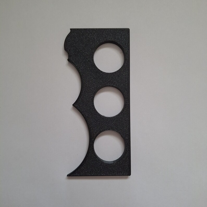 Peut inclure: Un outil noir, rectangulaire et textur&eacute; pr&eacute;sentant trois d&eacute;coupes circulaires dispos&eacute;es verticalement au centre et une s&eacute;rie de trois indentations incurv&eacute;es en forme de feston le long d'un des bords longs, cr&eacute;ant un profil distinctif.