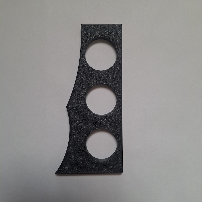 Puede incluir: Un panel vertical de color gris oscuro con textura que presenta tres recortes circulares dispuestos en columna. El borde izquierdo del panel tiene un perfil curvo y asim&eacute;trico, mientras que el borde derecho es recto y definido.