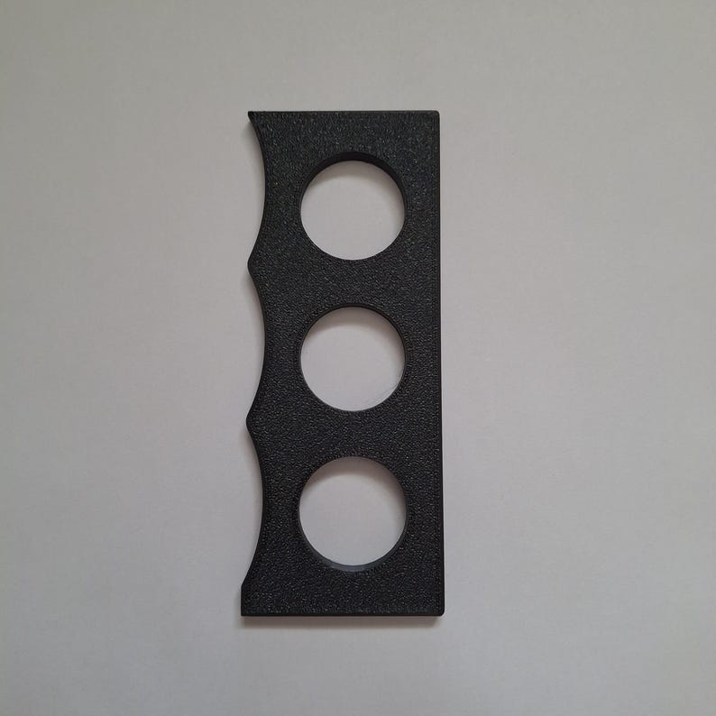 May include: A rectangular black object with a textured surface featuring three circular cutouts arranged vertically in the center and a scalloped edge on the left side. The item is flat and has a straight edge on the right side.