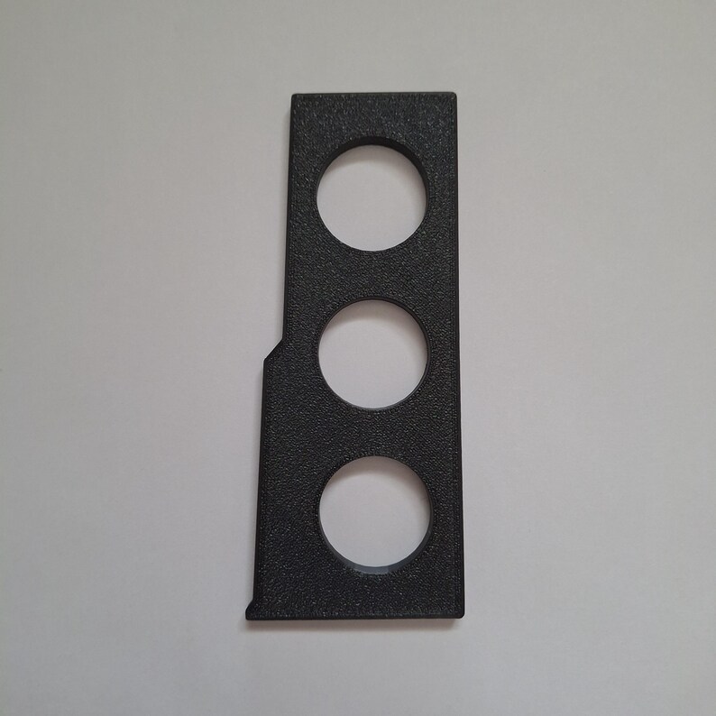 May include: A rectangular black panel with a textured surface featuring three evenly spaced circular cutouts arranged vertically. The panel has a straight right edge and a slightly angled left edge, creating a tapered shape at the top and bottom.