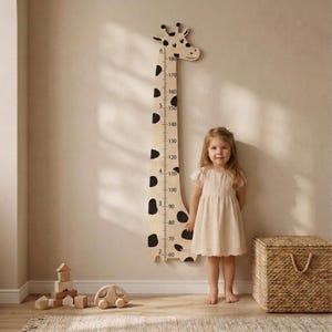 May include: A wooden giraffe-shaped height chart with black spots and markings in centimetres. The chart is mounted on a beige wall. A young child stands next to the chart. A woven basket and wooden toys are in the foreground.