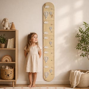 May include: A wooden height chart featuring hot air balloon and cloud cutouts. The chart measures up to 150 inches (381 cm) and is decorated with white clouds and hot air balloons. A young child stands next to the chart.