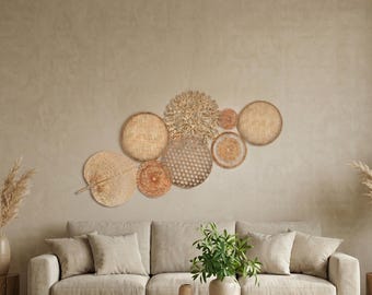 Könnte beinhalten: Eine Sammlung gewebter Wanddekorationen in verschiedenen Formen und Größen, darunter Kreise und ein Fächer, in natürlichen Beige- und Brauntönen. Die Anordnung ist an einer neutralfarbenen Wand über einem beigen Sofa und einem Holztisch angebracht und schafft eine warme Atmosphäre.