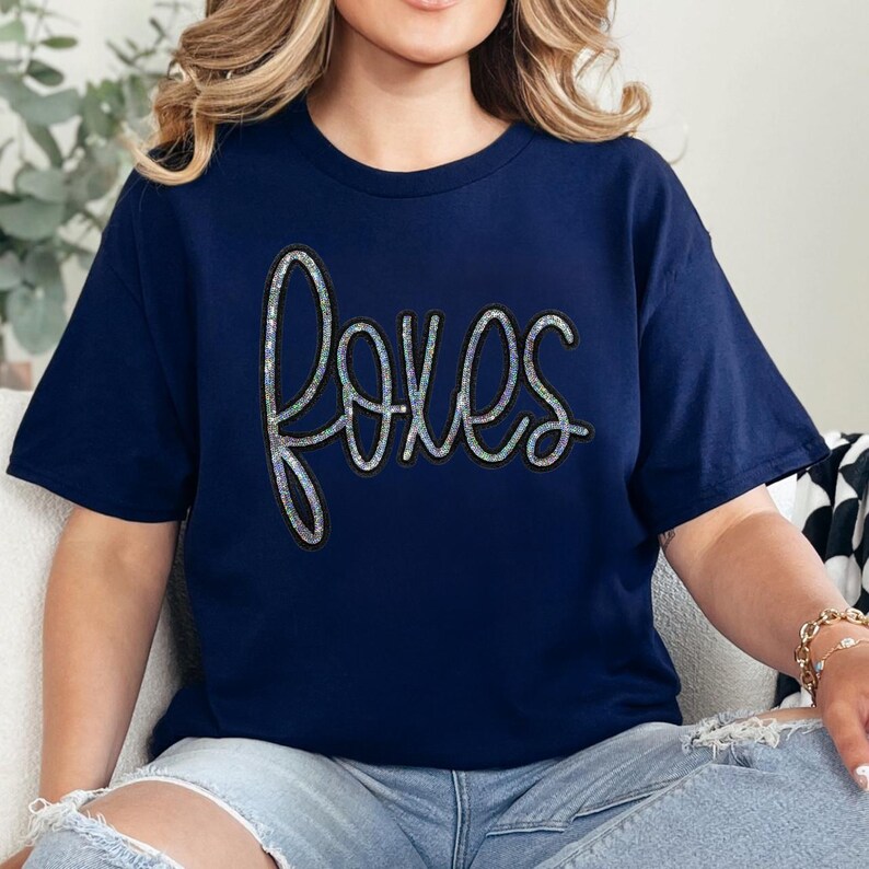 Product Foxes Sequin Patch, a sparkling sequin embroidered patch of the word "foxes" on a navy blue t-shirt.