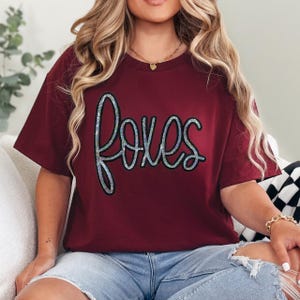 Foxes Sequin Patch, glittering sequin patch spelling 'Foxes' on a maroon t-shirt.