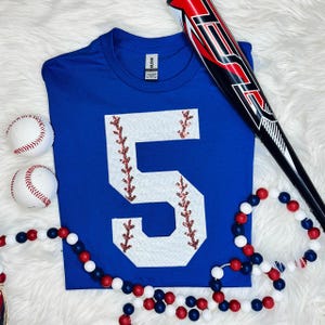 Baseball Number Sequin Patch, close-up of a number six sequin patch on a blue shirt with baseball-themed items around it.