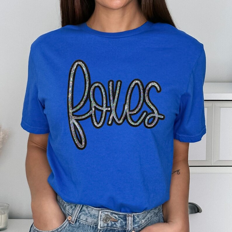Foxes Sequin Patch, close-up of a vibrant blue t-shirt with a sparkling sequin patch spelling 'foxes' in a playful, cursive font.