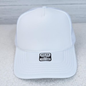 White Foam Trucker Hat, front view of a white foam trucker cap with a mesh back and a black and white label on the bill reading 'OTTO WORLD FAMOUS FOAM FRONT TRUCKER'.