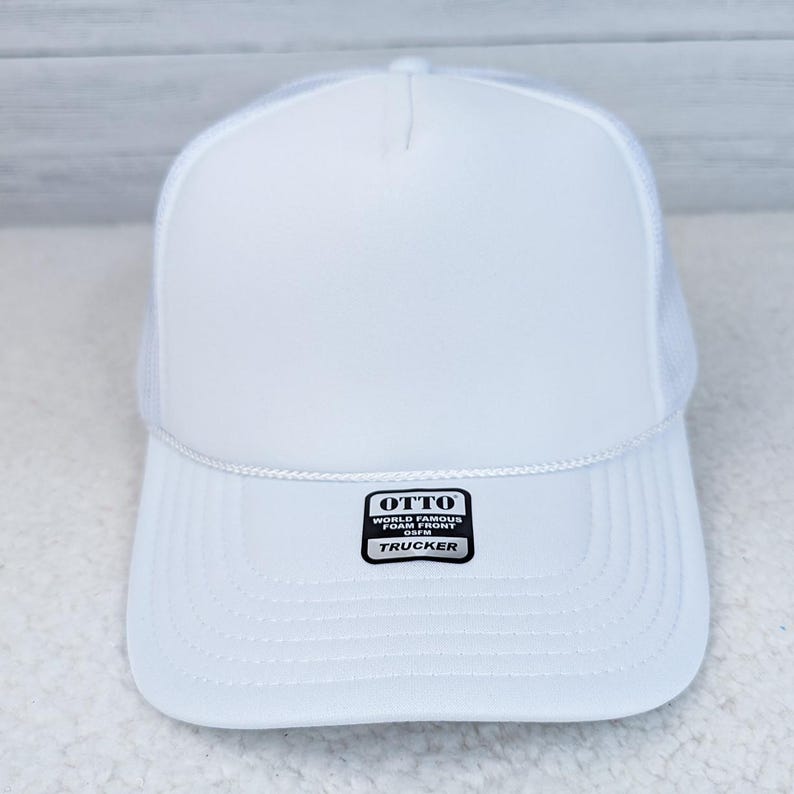 White Foam Trucker Hat, front view of a white foam trucker cap with a mesh back and a black and white label on the bill reading 'OTTO WORLD FAMOUS FOAM FRONT TRUCKER'.