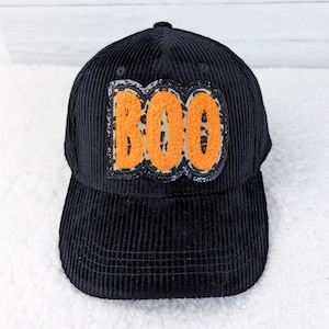 May include: Black corduroy baseball cap with the word "BOO" in orange letters with a leopard print design. The hat has a curved brim and a structured crown, perfect for Halloween.