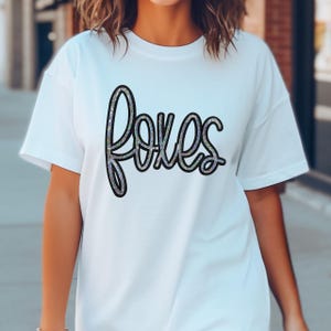 Foxes Sequin Patch, close-up of white T-shirt with black and multicolored sequin word 'foxes' on the front.