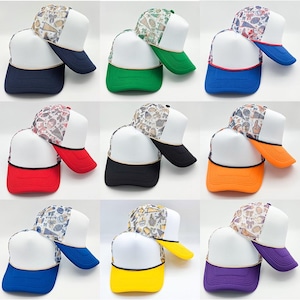 May include: A collection of nine foam-front trucker hats, each featuring a white front panel, a mesh back panel with a sports-themed print, and a solid-colored brim. The hats are displayed in various color combinations including navy, green, blue, red, black, orange, and yellow.
