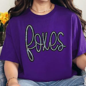Foxes Sequin Patch, a close-up of a purple t-shirt with a colorful, shiny sequin applique spelling 'foxes' in a cursive font.