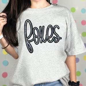 Foxes Sequin Patch, a decorative sequin patch shaped like a fox on a light grey T-shirt with the word 'foxes' written in cursive.