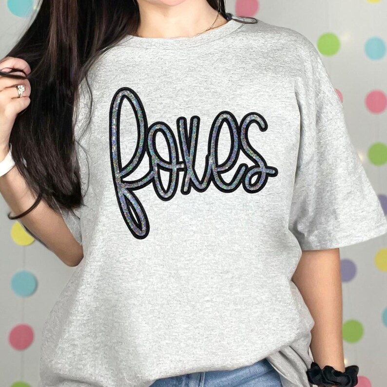Foxes Sequin Patch, a decorative sequin patch shaped like a fox on a light grey T-shirt with the word 'foxes' written in cursive.