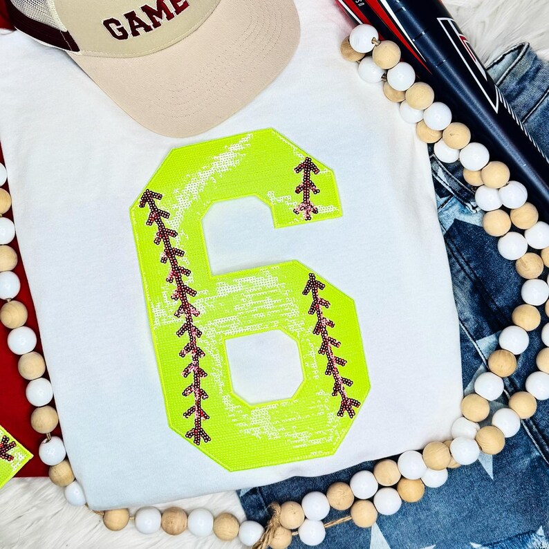 Softball Number Sequin Patch, bright neon yellow number six with black and pink embroidery details, on a white T-shirt.
