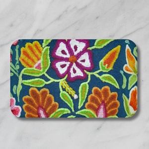 May include: A rectangular, navy blue decorative mat with a floral design. The embroidered flowers are in shades of orange, yellow, pink, and white, with green leaves and stems. The mat has rounded corners.