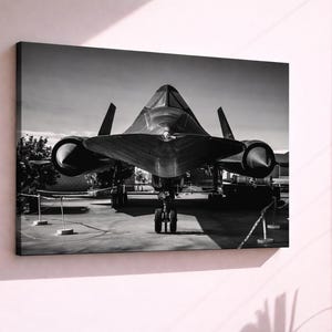 May include: Black and white canvas print of an SR-71 Blackbird aircraft. The jet is positioned head-on, showcasing its sleek, aerodynamic design. The image captures the aircraft's distinctive shape, including its long fuselage, delta wings, and twin engines.