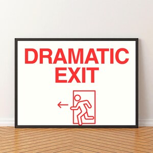 May include: A framed print with the words "DRAMATIC EXIT" in red block letters. Below the text is a red graphic of a person running towards an exit door with an arrow pointing left. The frame is black.
