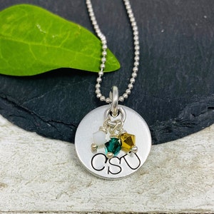 May include: A silver pendant necklace with a round charm. The charm has the letters "CSU" stamped on it, with three small, colorful crystals hanging below. The necklace chain is a ball chain.