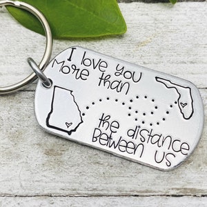 May include: Silver keychain with a map of Georgia and Florida, connected by a dotted line. The keychain says "I love you more than the distance between us".