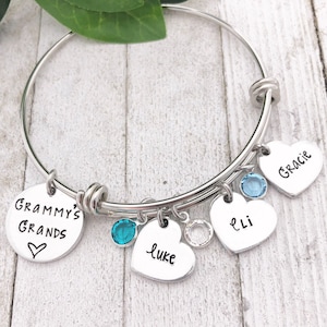 May include: A silver adjustable bracelet with heart-shaped charms. The charms are engraved with names and accented with blue and clear crystals. One charm reads "Grammy's Grands."
