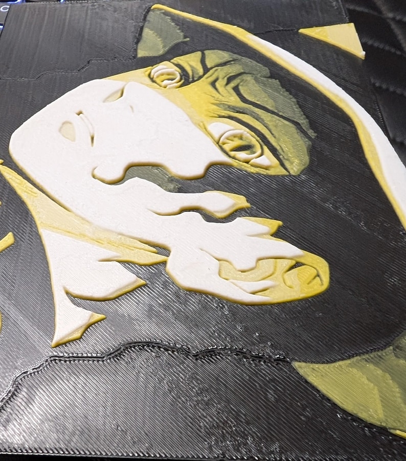 May include: A 3D-printed artwork depicting a stylized face with white and yellow details on a black background. The piece has a textured surface, resembling a relief sculpture.