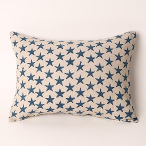 May include: A rectangular pillow with a cream-colored background and a pattern of dark blue stars. The stars are evenly spaced across the surface of the pillow, creating a repeating design. The pillow has a soft, inviting appearance.