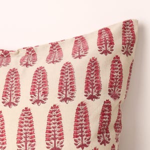 Könnte beinhalten: Cremefarbenes Kissen mit einem sich wiederholenden Muster aus roten floralen Designs. Das florale Muster ist eine stilisierte, vertikale Anordnung von Blättern und Blüten. Das Kissen hat ein weiches, strukturiertes Aussehen.