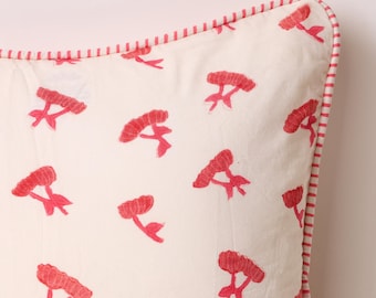 May include: Cream-colored square pillow with a repeating pattern of red floral embroidery. The pillow has a red and white striped border, adding a decorative touch. The floral design gives the pillow a fresh, spring-like feel.